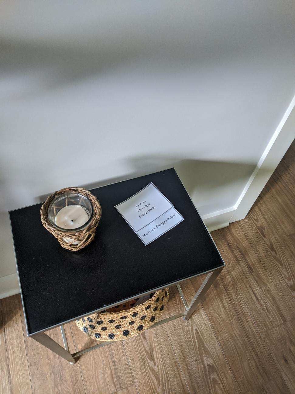 Black side table with a candle, paper, and leopard-print basket on wood floor, against a white wall.