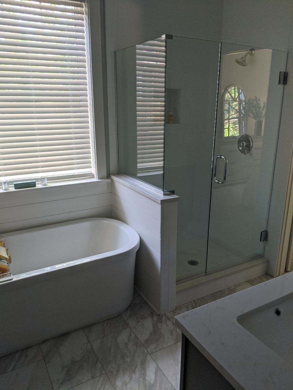 Bathroom with a white tub, glass shower, and white vanity with window blinds.