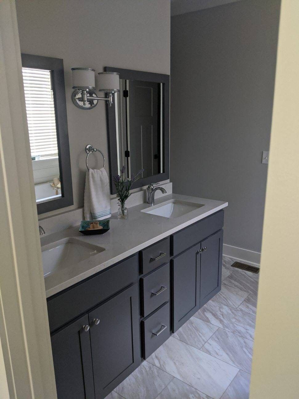 Bathroom with gray vanity, white countertop, two sinks, framed mirrors, and silver fixtures.