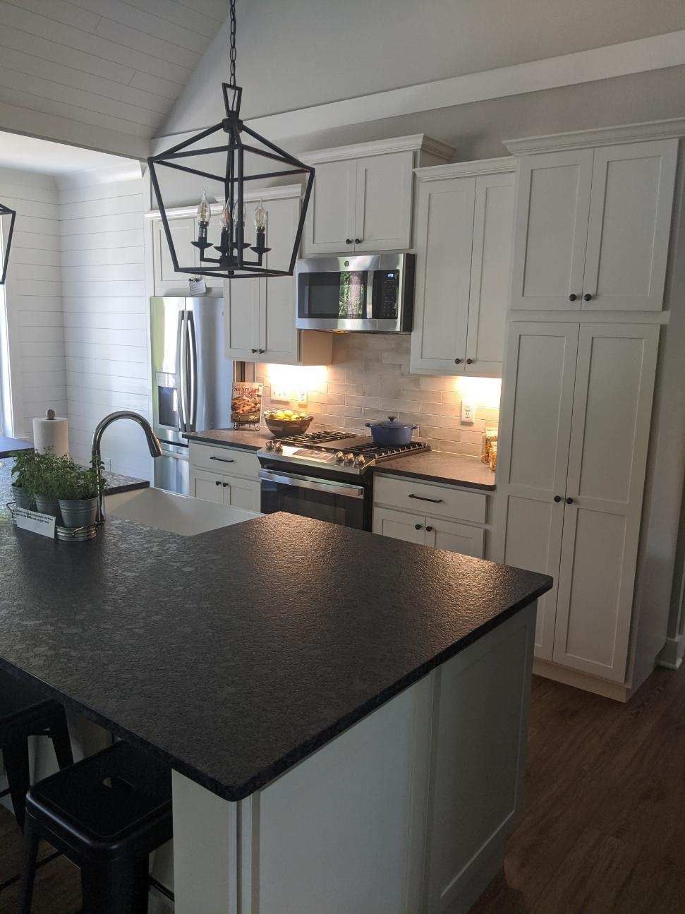 White kitchen with dark countertops, stainless steel appliances, and a black lantern.