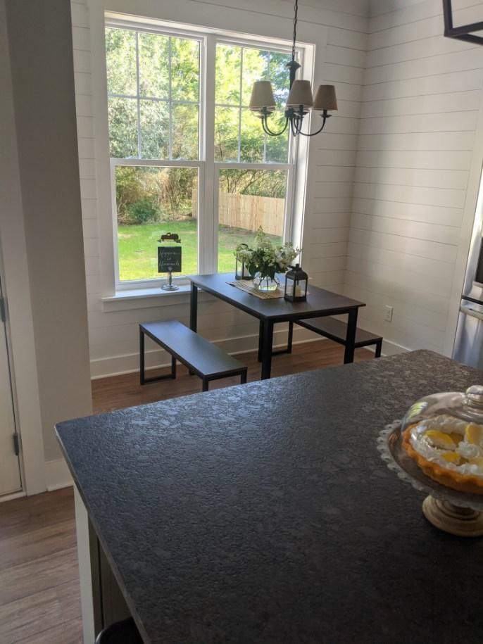 Dining area with dark table and bench under window, white shiplap wall, and granite countertop.