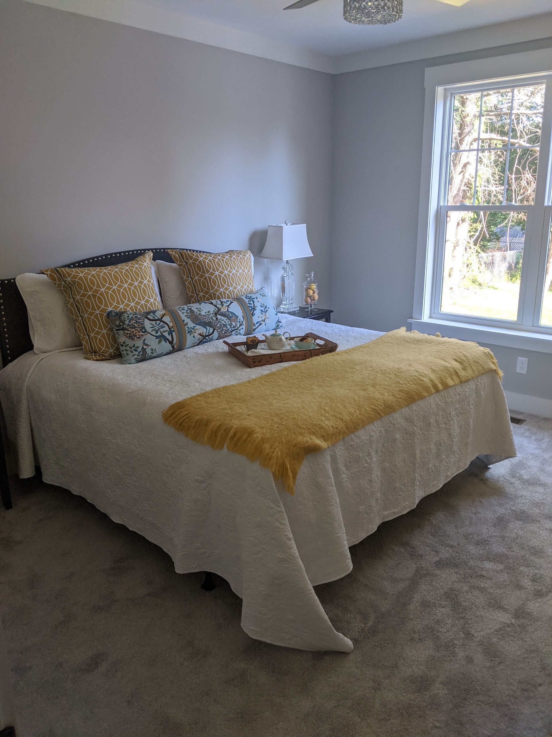Bedroom with a bed, pillows, and throw; window on the right. Gray walls and carpet.