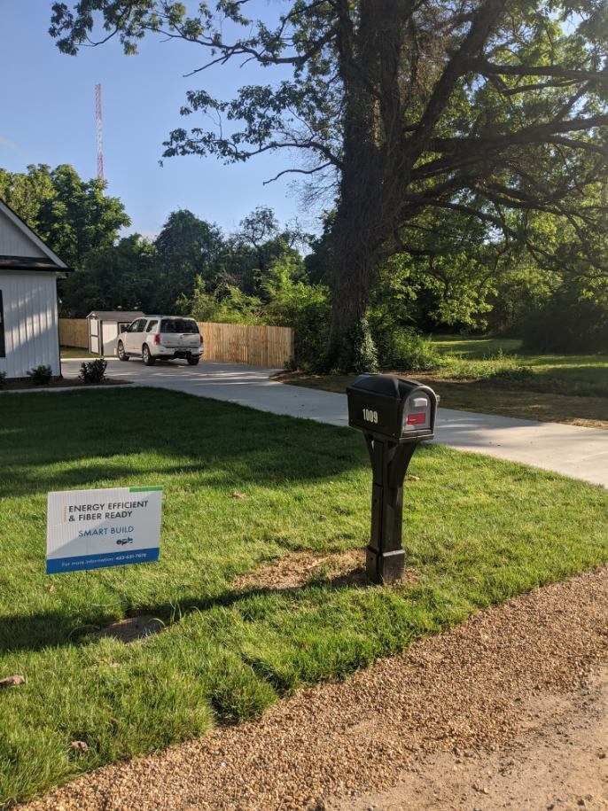 A house with a sign, mailbox, driveway, and trees in a yard.