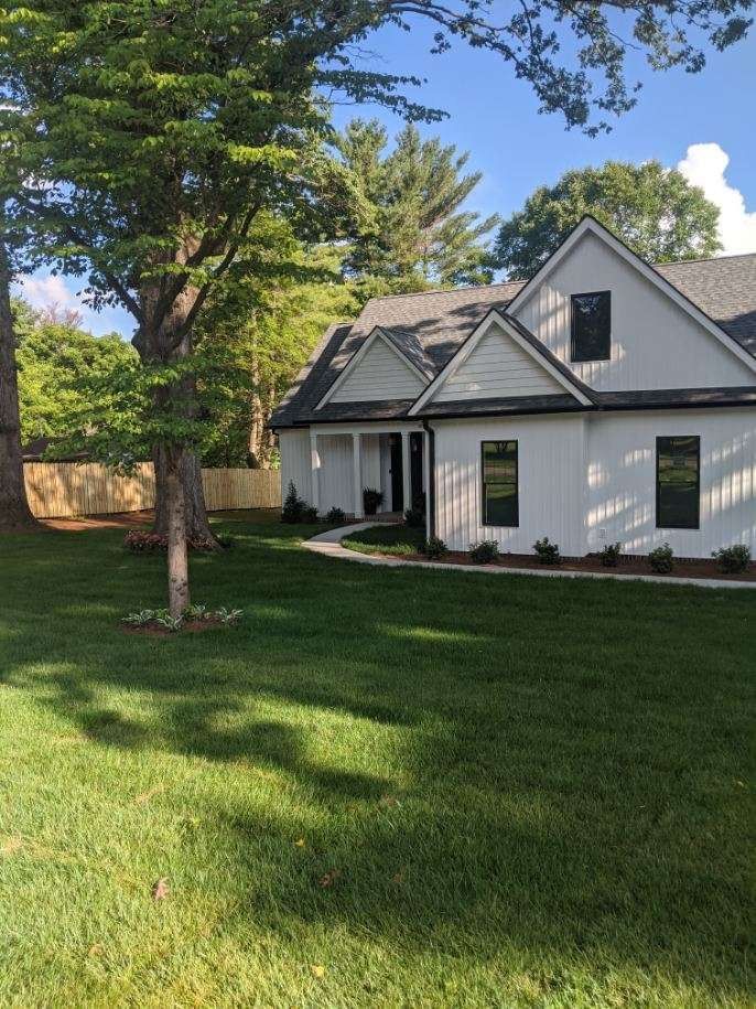 White house with black trim, green lawn, and trees under a blue sky.