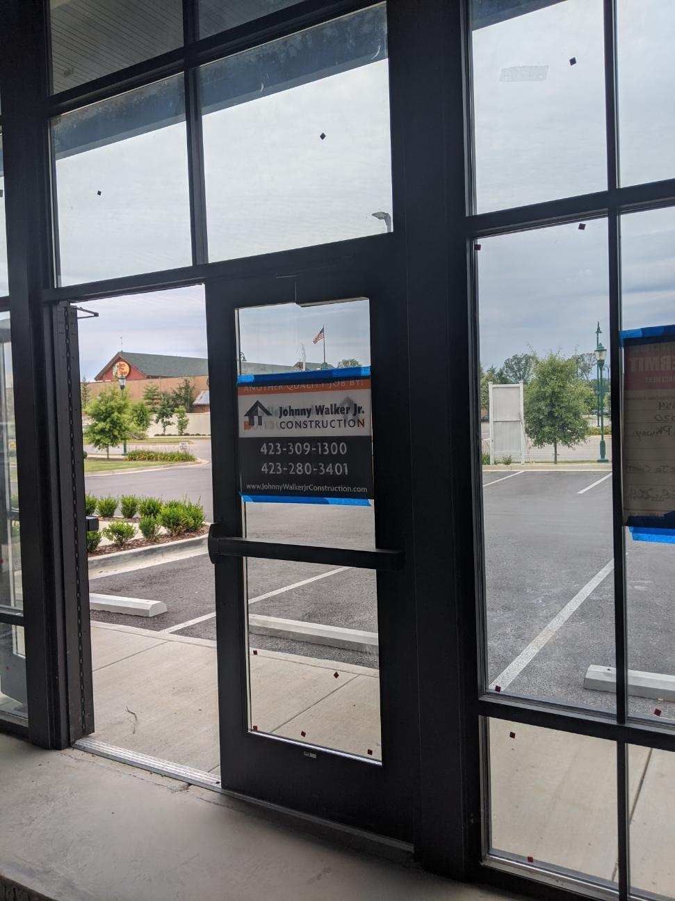 Exterior door with a business sign and surrounding windows, a parking lot and sky visible.