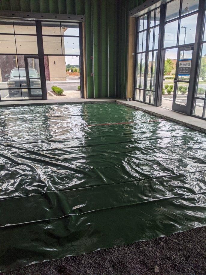 Green tarp with standing water inside building with large windows; gravel floor.