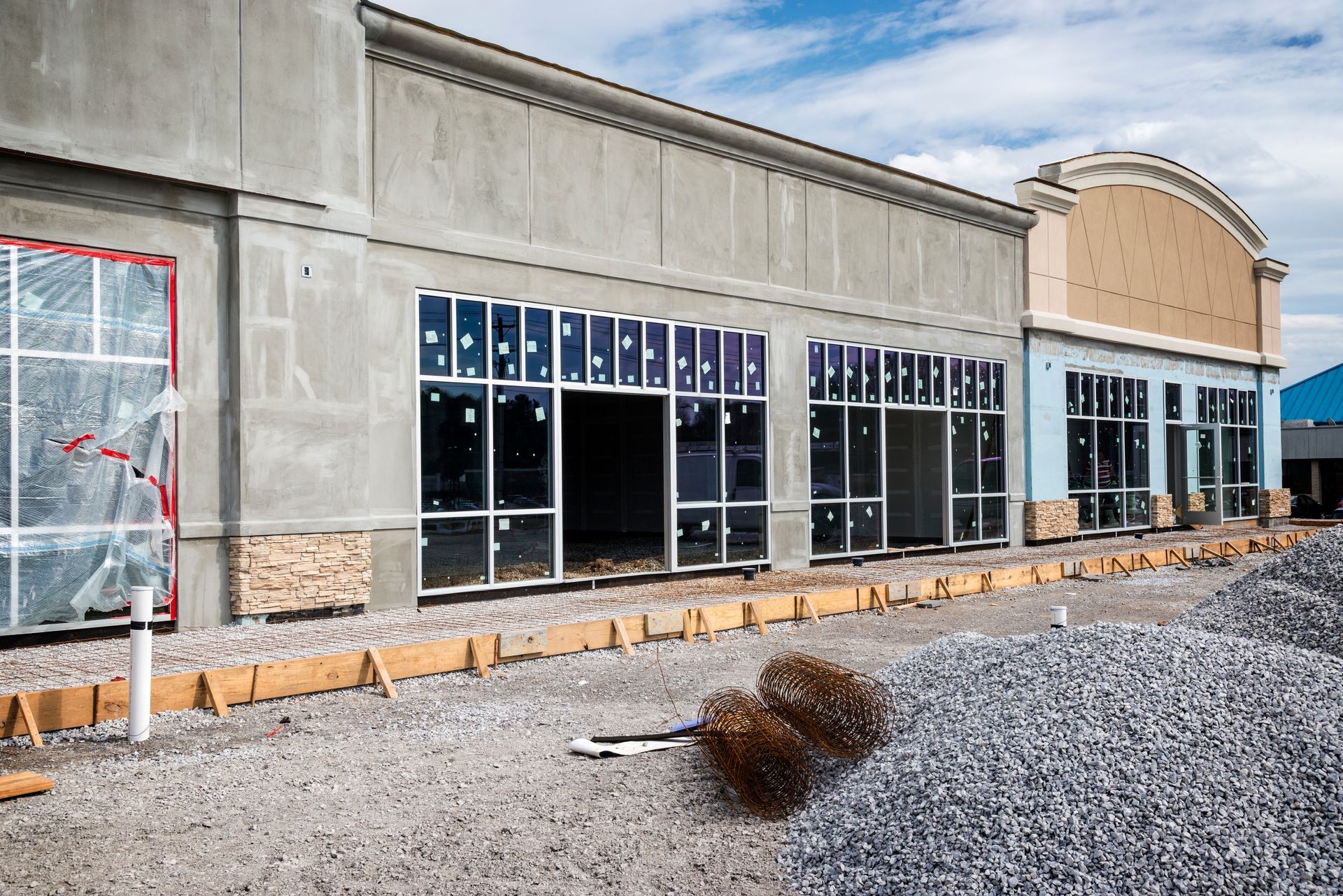 Construction of a commercial building, unfinished exterior with glass windows and stone and gravel ground.