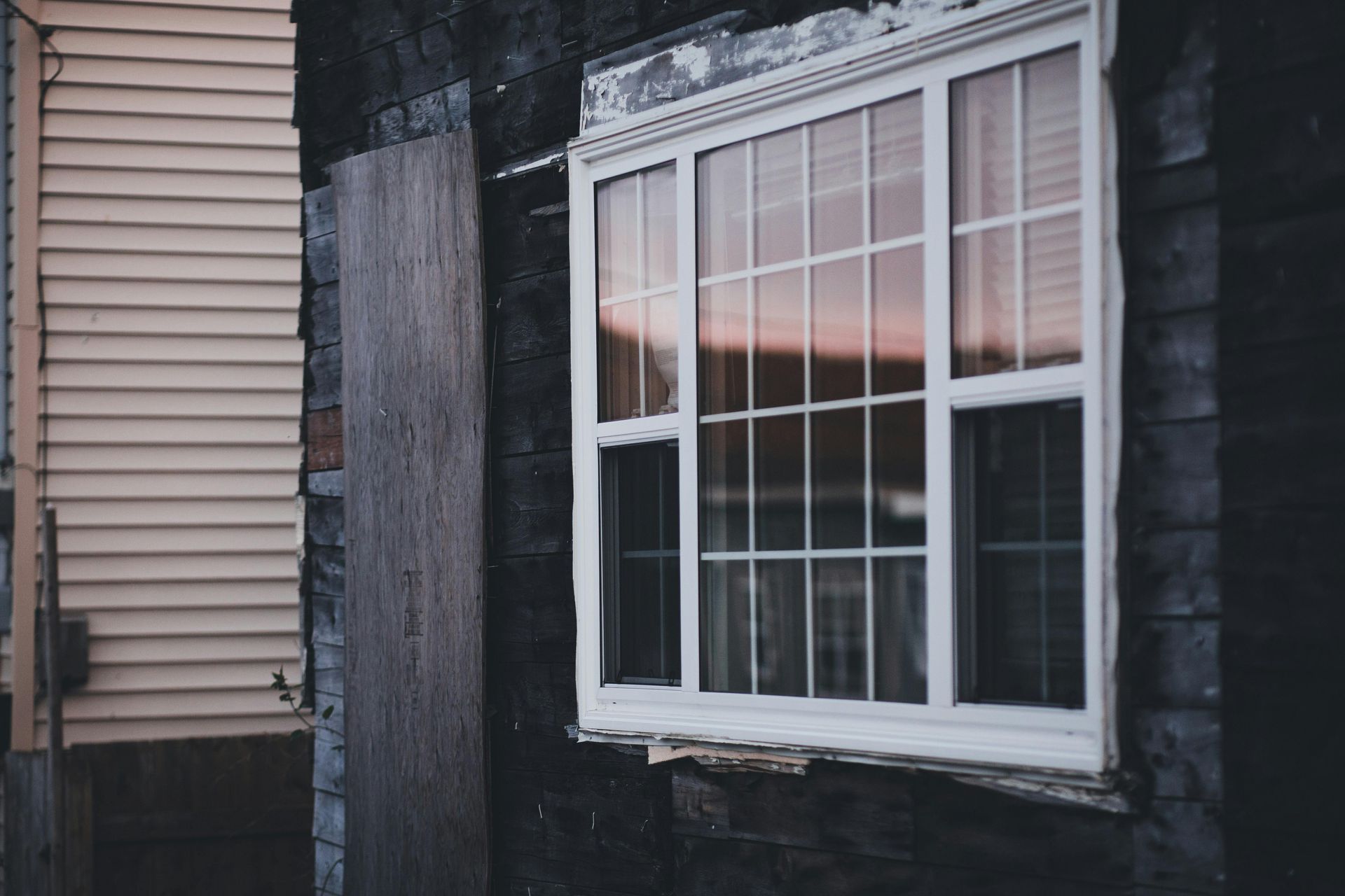 White-framed window with grid panes on a dark exterior wall, reflecting a pink sunset.