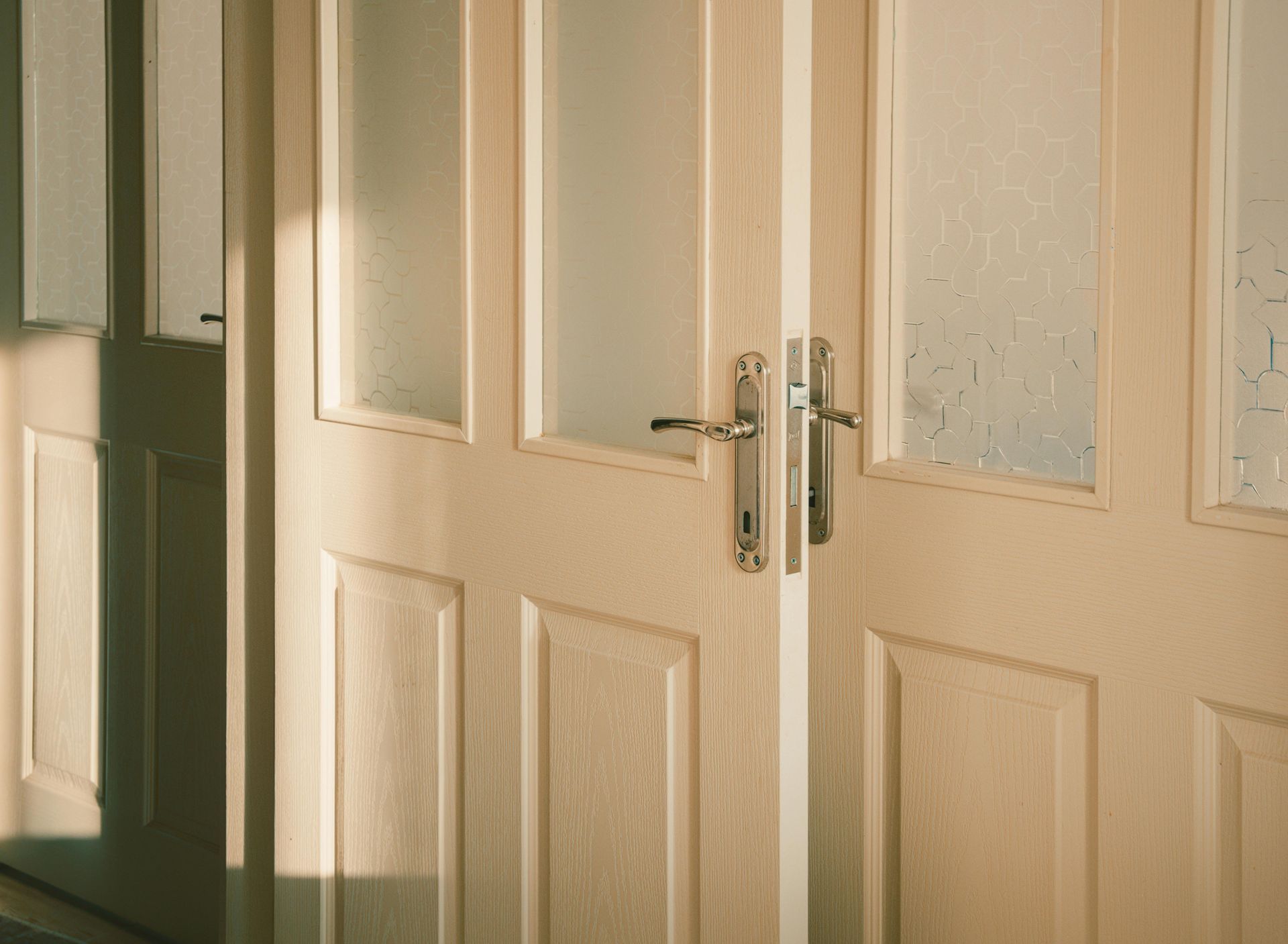 Double wooden doors with frosted glass panels in a softly lit interior hallway