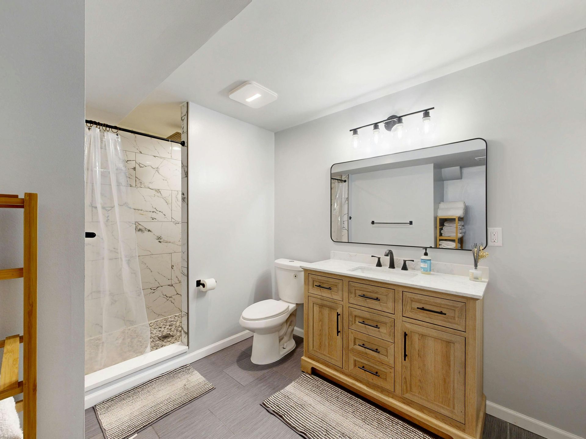 Modern bathroom with glass shower, toilet, wood vanity, large mirror, and light gray walls