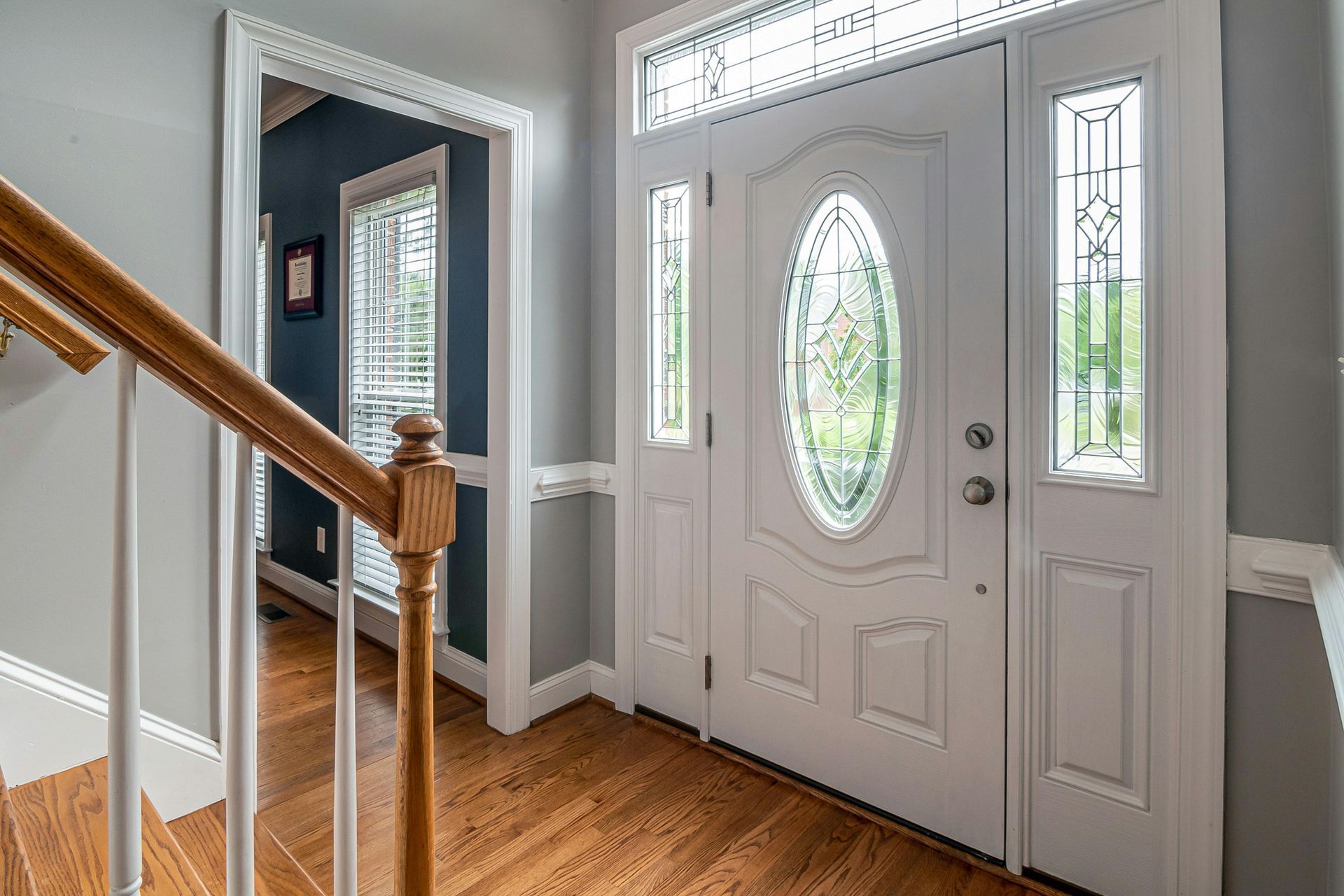 Front entryway with white door, oval glass insert, hardwood floor, and staircase railing