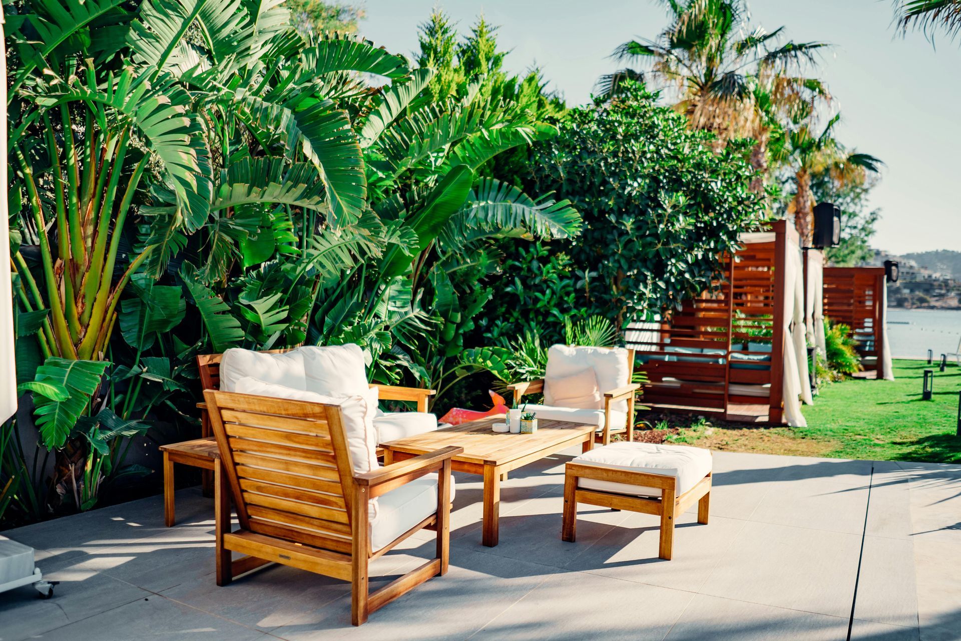 Wooden patio chairs and table beside a lush tropical garden and poolside walkway