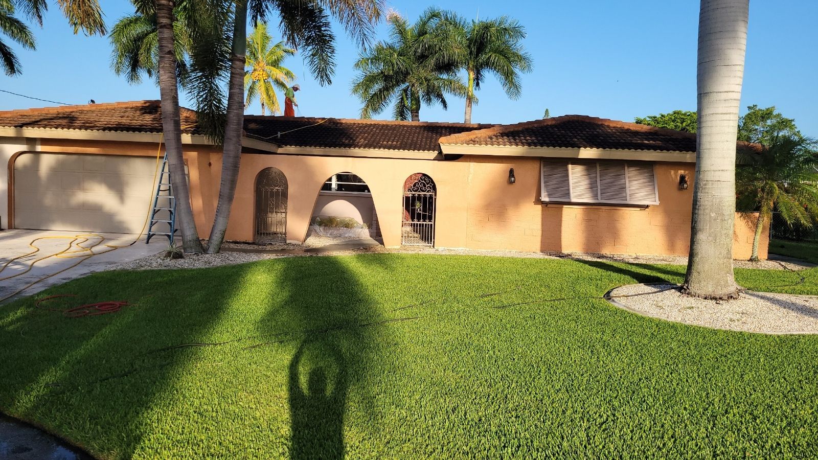 A shadow of a person is cast on the grass in front of a house.
