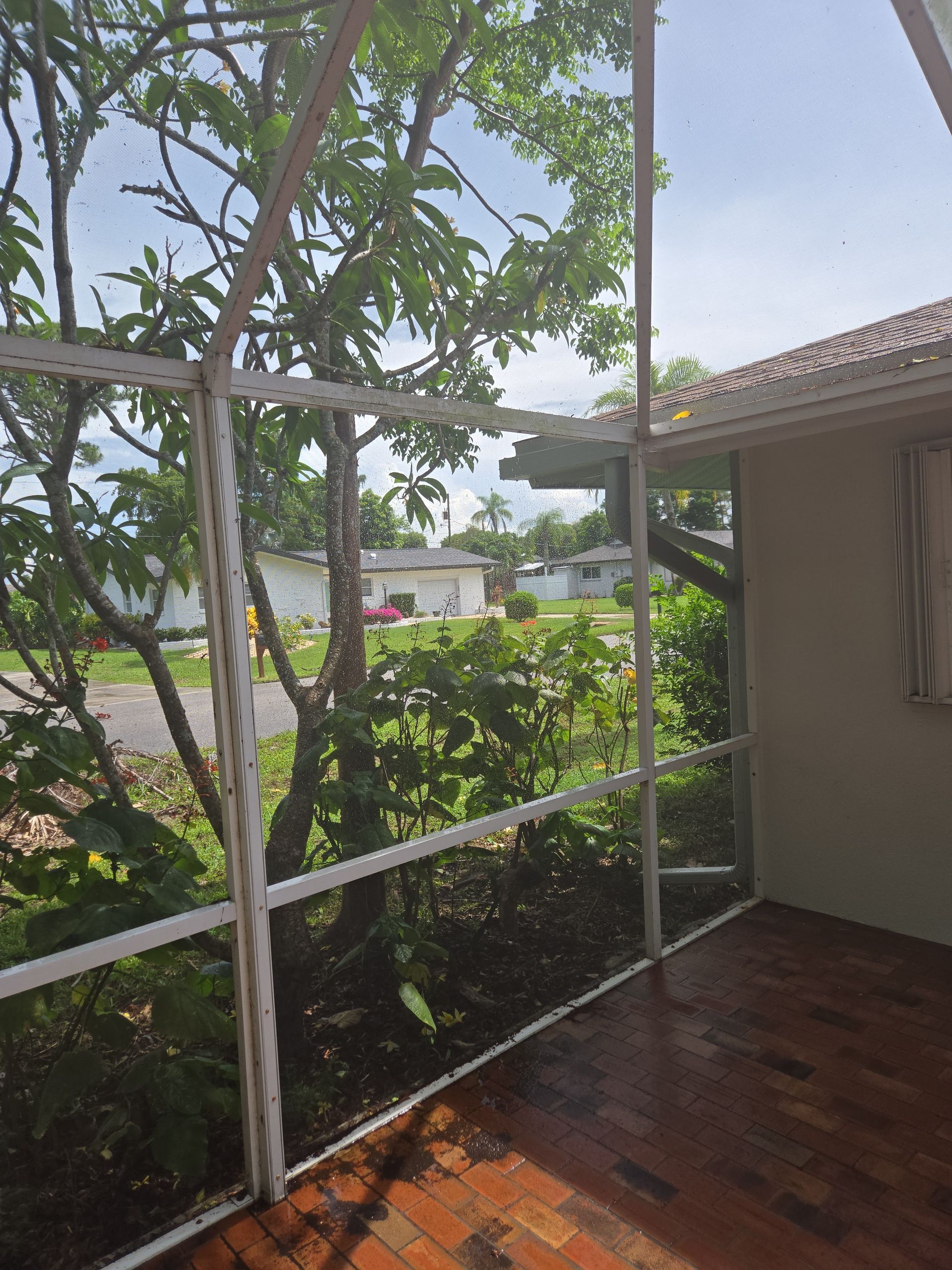 A screened in porch with a view of trees and a house in the background.