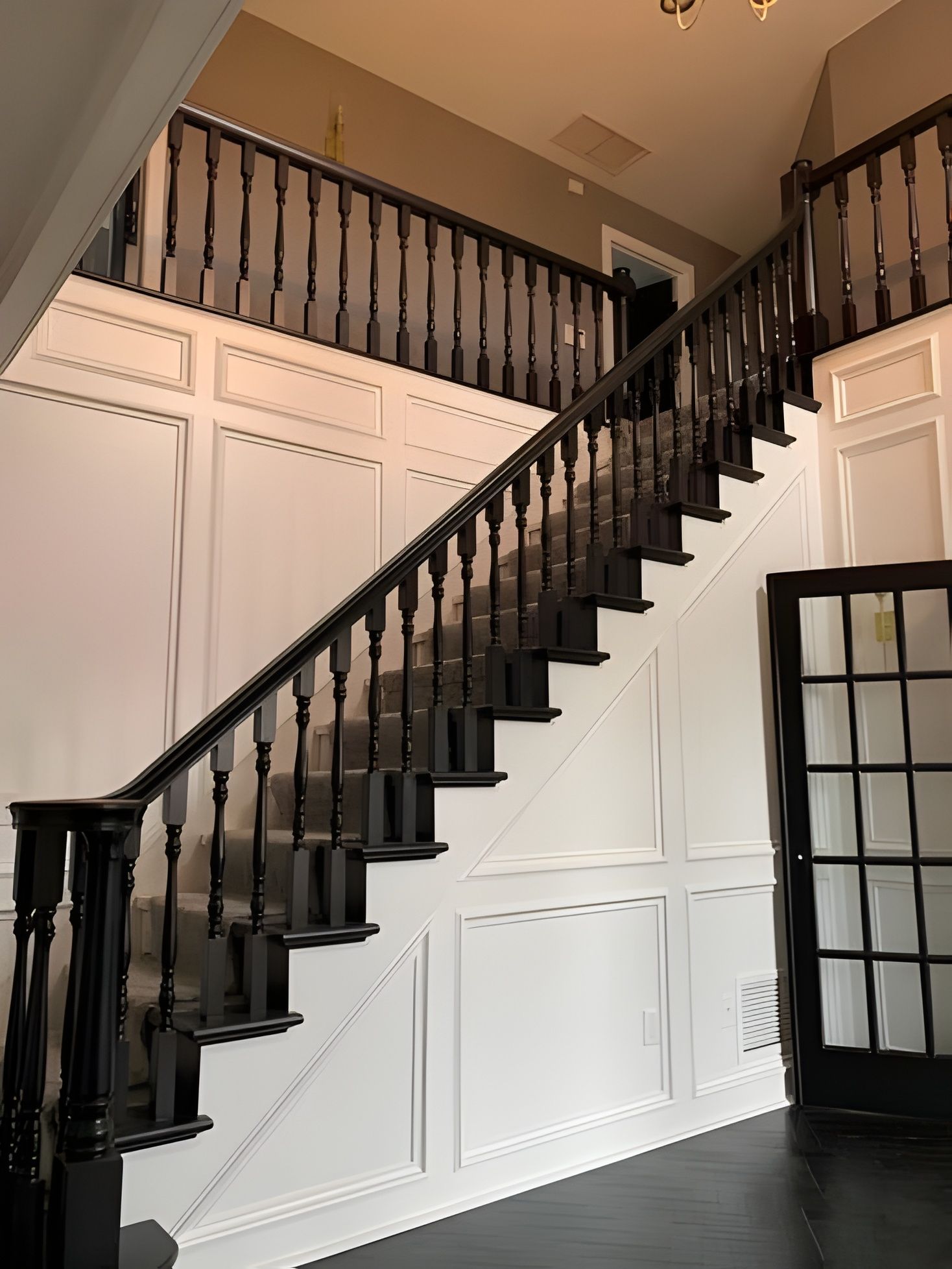 A grand foyer featuring a staircase with black wooden railings, white paneled walls, and dark hardwood floors.