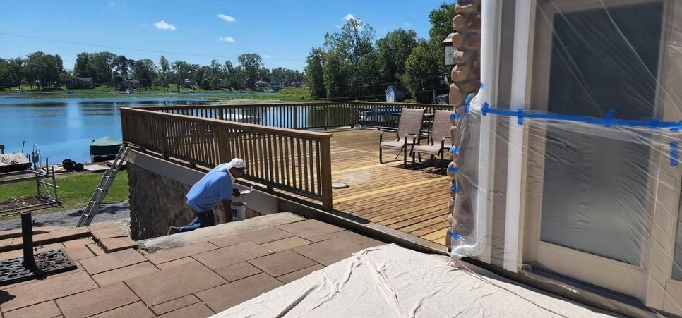 A person in a blue shirt works on an outdoor deck overlooking a lake on a sunny day.