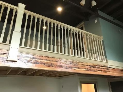 A white wooden railing lines an interior mezzanine balcony above a rough-hewn wooden support beam and white wall.