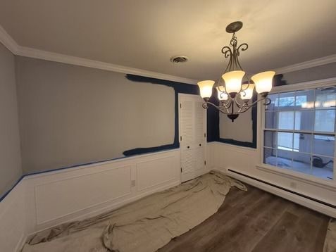 A room with gray walls partially painted navy blue, white wainscoting, a chandelier, and a drop cloth on the floor.