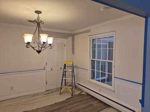 A room under renovation with white wainscoting, grey paint on an upper wall, blue painter's tape, and a step ladder.