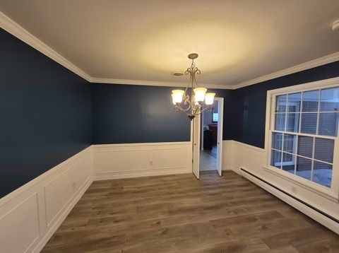 A dining room with dark navy walls, white wainscoting, a crystal chandelier, and light wood floors.