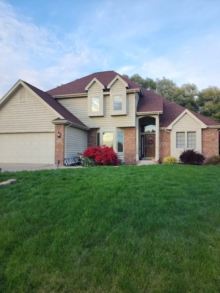 A two-story suburban house with a brick and beige exterior, a multi-gabled roof, and a green front lawn.