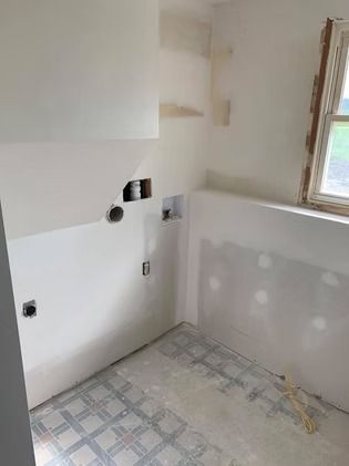 A small, unfinished laundry room with white walls, patterned tile flooring, and exposed utility hookups.