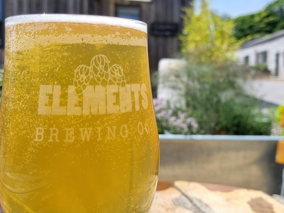 A glass of beer from elements brewing company is sitting on a table.