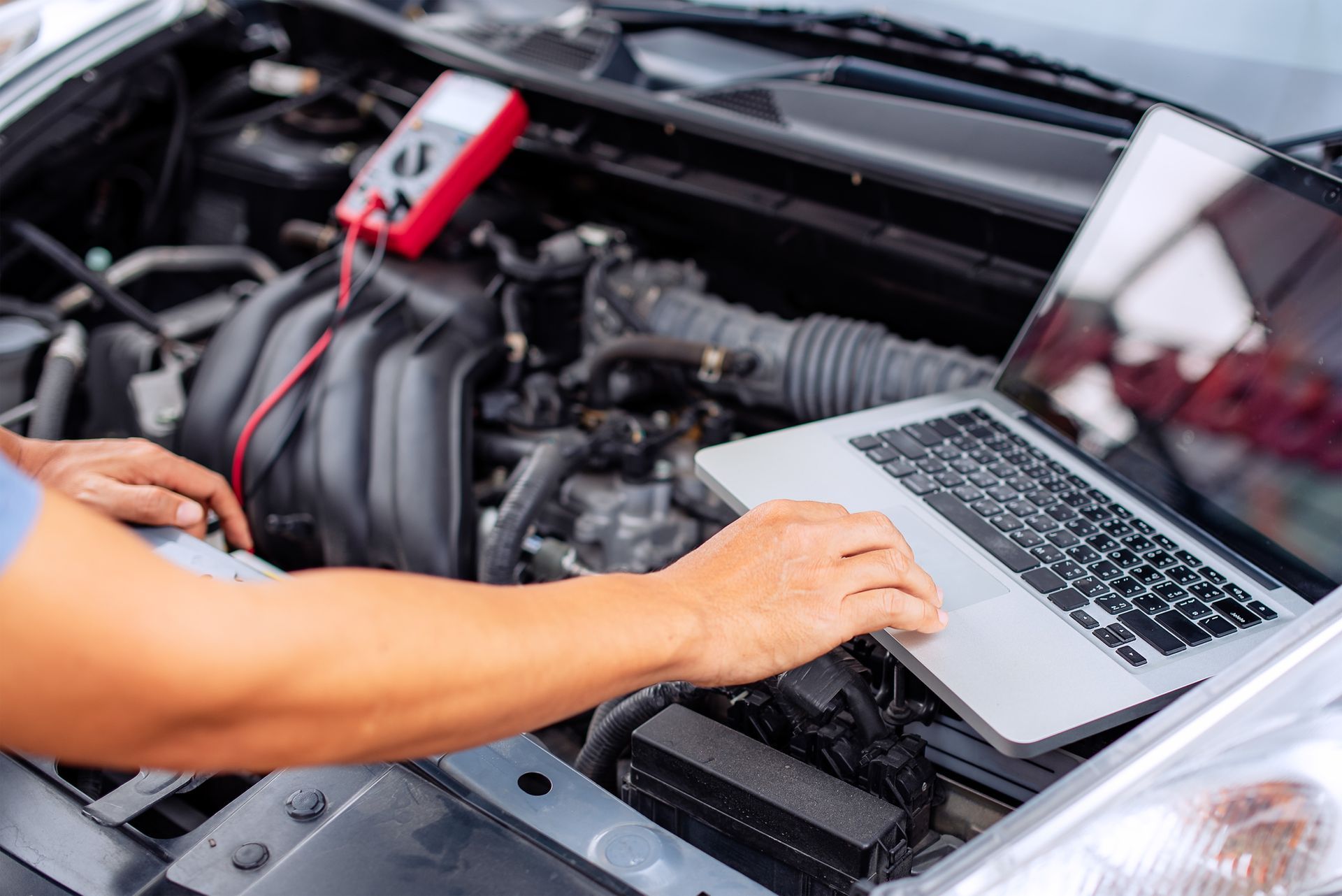 A man is using a laptop computer under the hood of a car.
