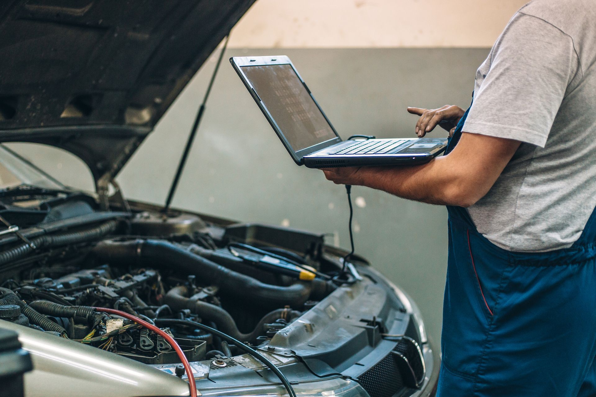 A man is using a laptop computer while working on a car.