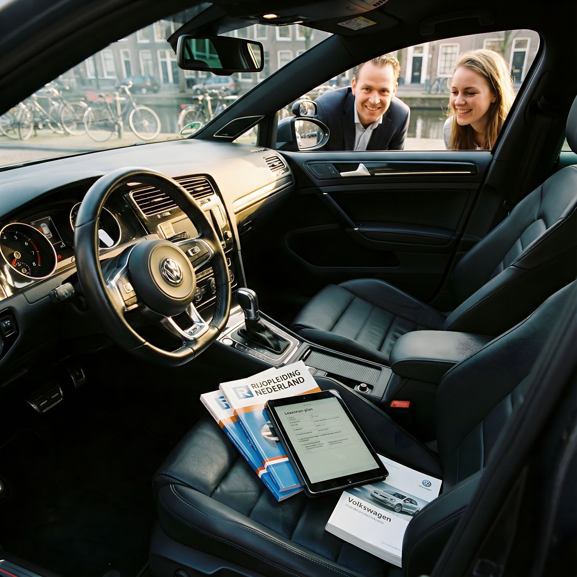 Interieur van een auto met een stel dat naar binnen kijkt. Zwarte lederen stoelen, stuurwiel en navigatie op de middenconsole.