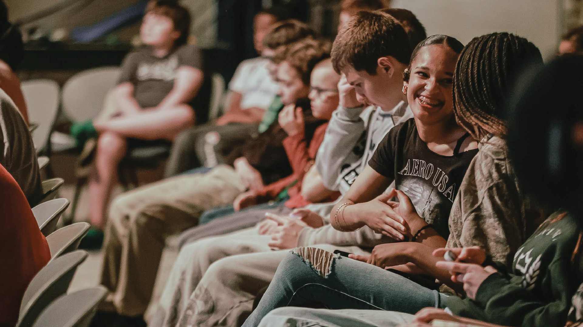 Audience seated in chairs, chatting and smiling during an indoor event