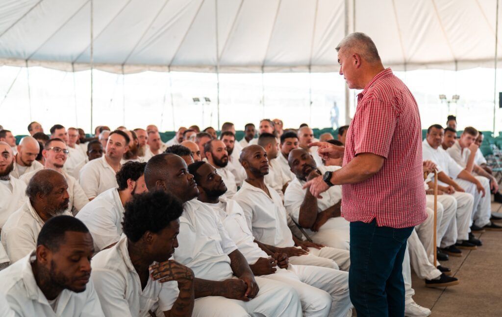 Man speaking to a seated audience inside a large white event tent
