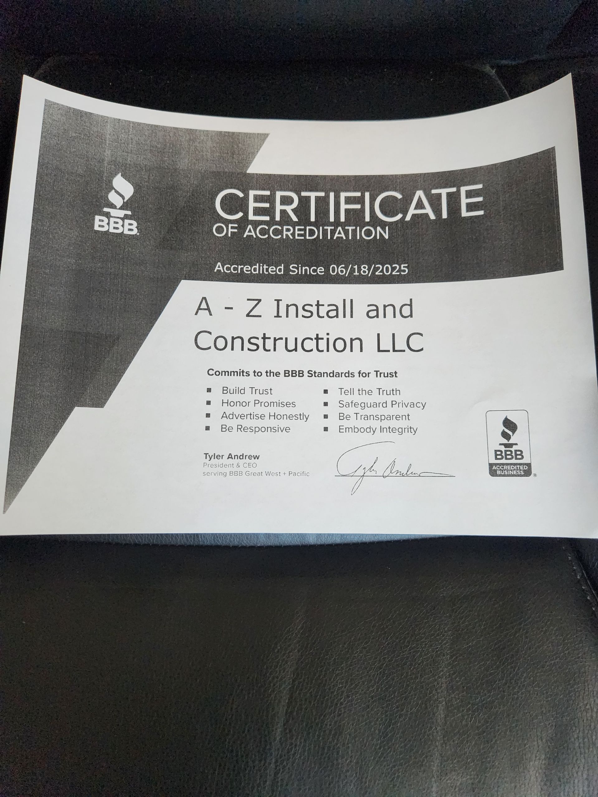 Certificate of Accreditation for A-Z Install and Construction LLC, listing services with a logo, on a black surface.