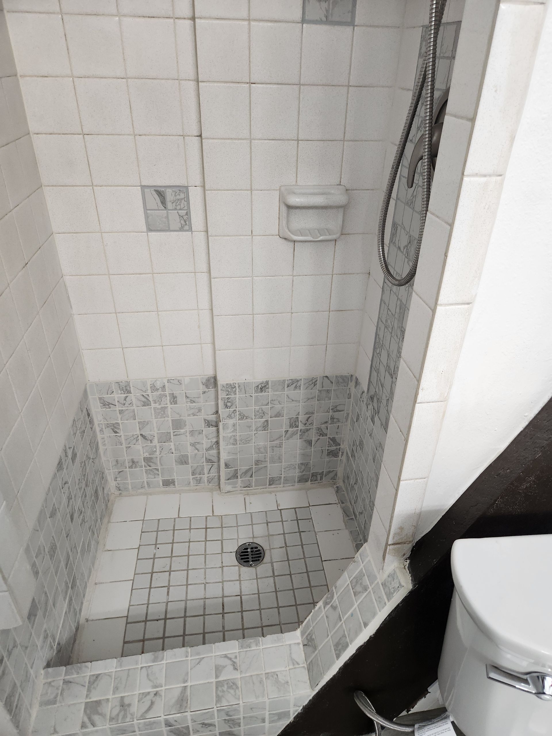 Small white tiled shower with mosaic lower walls, soap dish, and chrome showerhead.