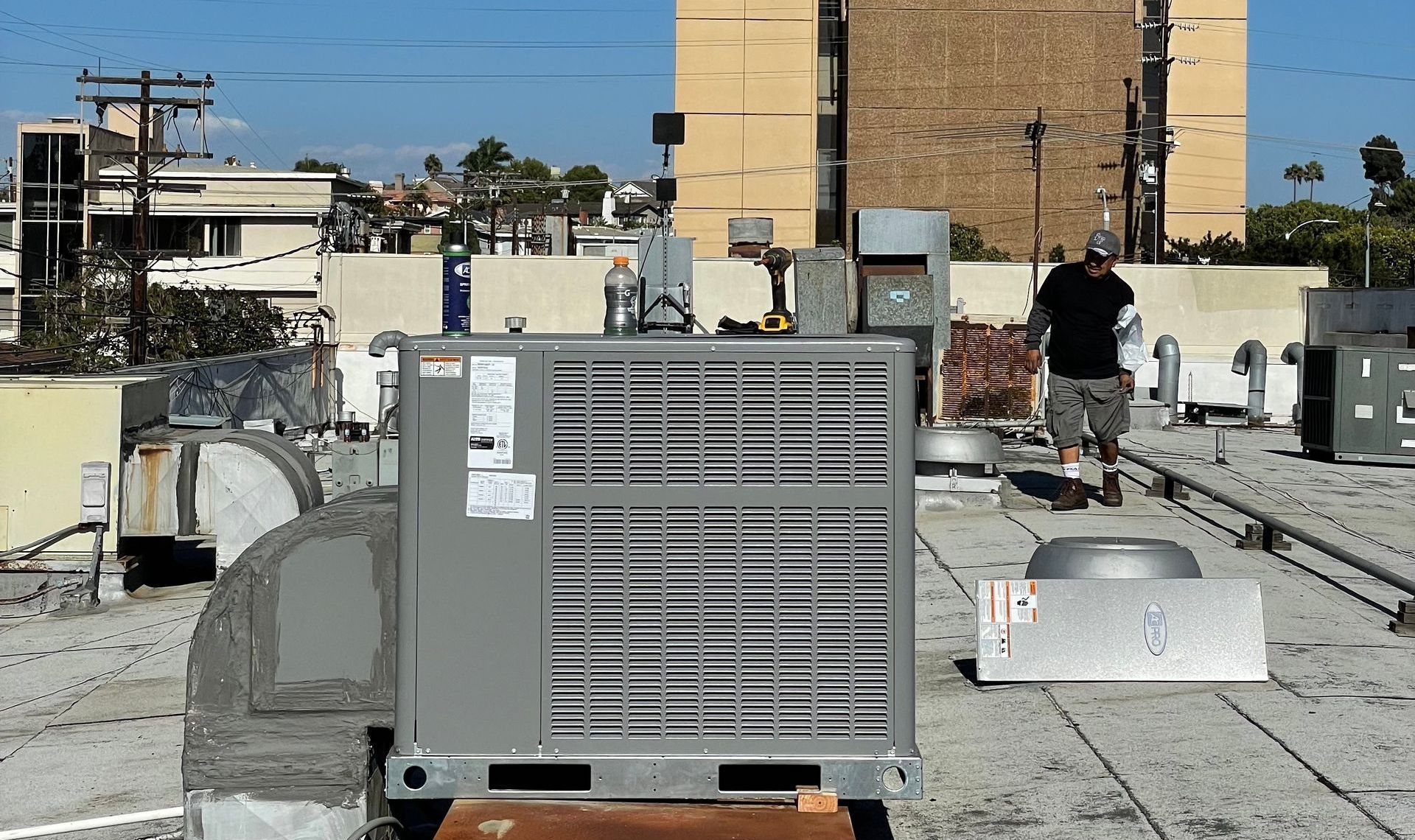 Man walking on a flat rooftop with HVAC equipment in the foreground under a clear, sunny sky.