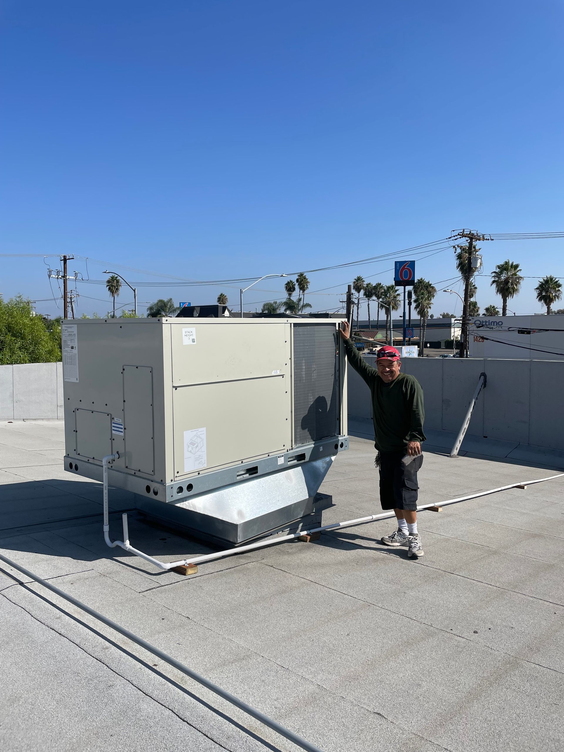 Man stands next to a large, rectangular HVAC unit on a rooftop under a clear, blue sky.