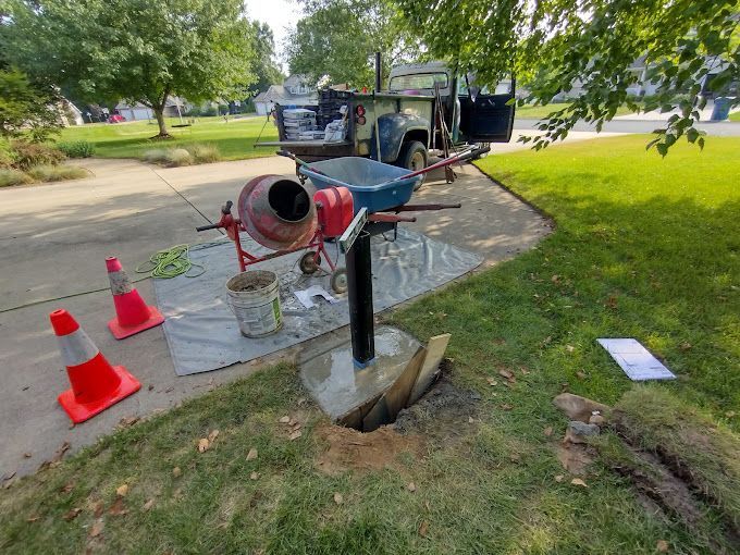 A concrete mixer is sitting next to a post in the grass.