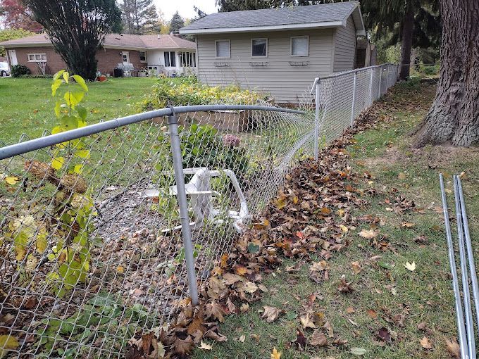 A chain link fence is surrounded by leaves and a house in the background.