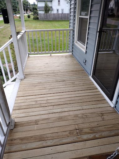 A wooden porch with a white railing and a sliding glass door.