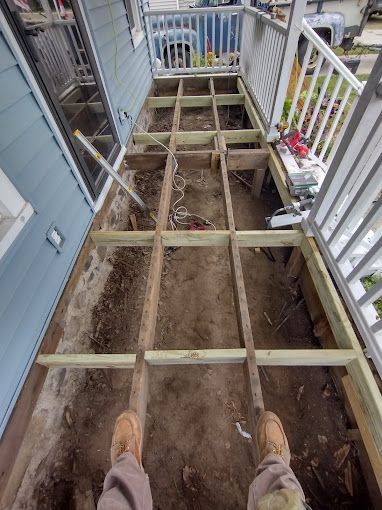 A person is standing on a wooden deck under construction.