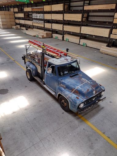 A blue truck with a ladder on top of it is parked in a warehouse.