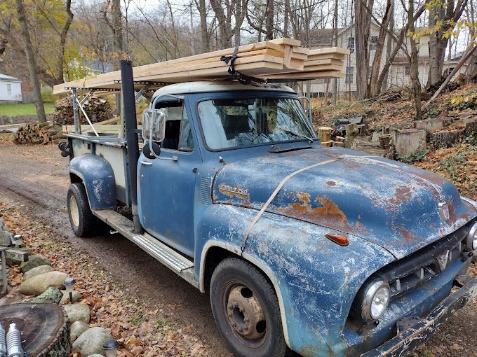 A blue truck with a stack of wood on top of it is parked on the side of the road.
