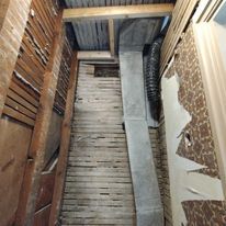 A room with a wooden floor and a concrete pipe coming out of the ceiling.