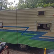 A green and white trailer is parked in a parking lot next to a motorcycle.