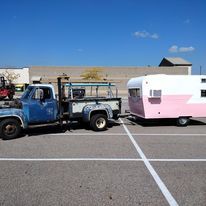 A blue tow truck is towing a pink trailer in a parking lot.