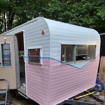 A pink and white trailer is parked in the woods.