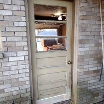 A white door with a glass window is on a brick wall.