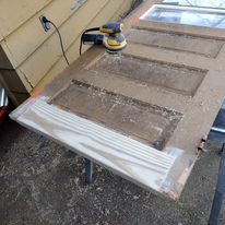A wooden door is being sanded with a sander.