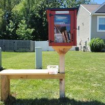 A small red box filled with books is sitting on top of a wooden bench.
