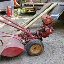 A red lawn mower is parked in the dirt next to a trailer.